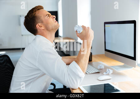 Wütend gestressten Jungunternehmer sitzen und zerknitterte Papier im Büro Stockfoto