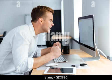 Wahnsinnig gereizt jungen Geschäftsmann sitzen und arbeiten mit leeren Bildschirm-Computer im Büro Stockfoto