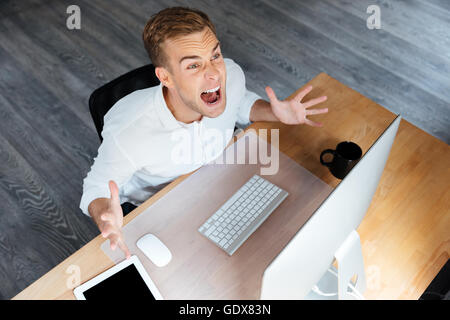 Draufsicht der verrückten irritiert junger Geschäftsmann arbeiten mit Computer und schreien Stockfoto