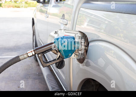 Gas-Pumpe-Düse in den Kraftstofftank eines Bronze Autos blau. Stockfoto