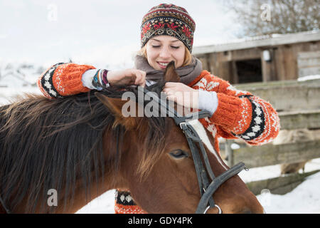 Junge Frau, die Anpassung der Trense ihr Pferd zum Reiten, Bayern, Deutschland Stockfoto