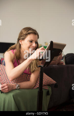 Junge Frau mit digital-Tablette in Wohnzimmer und lächelnd, München, Bayern, Deutschland Stockfoto