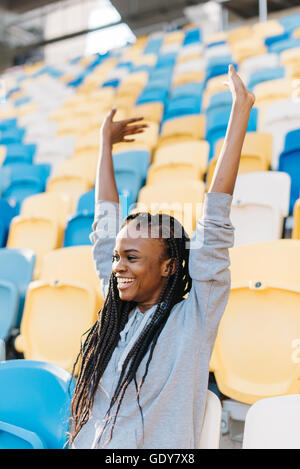 Glückliche junge afroamerikanische Frau graue Sportswear Team unterstützen oder Ziel auf große Stadion zu feiern Stockfoto