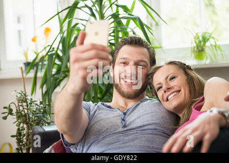 Paar Selfie in Wohnzimmer und lächelnd, München, Bayern, Deutschland Stockfoto