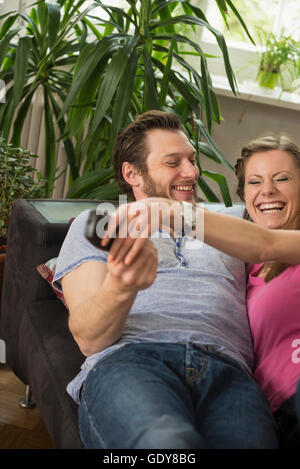 Paar kämpfen für Fernbedienung im Wohnzimmer, München, Bayern, Deutschland Stockfoto