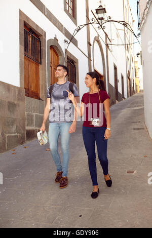 Niedliche Tourist paar im Urlaub mit einem Rucksack und Karte eine schmale Straße hinunter und zeigt während lässig in Jeans gekleidet Stockfoto