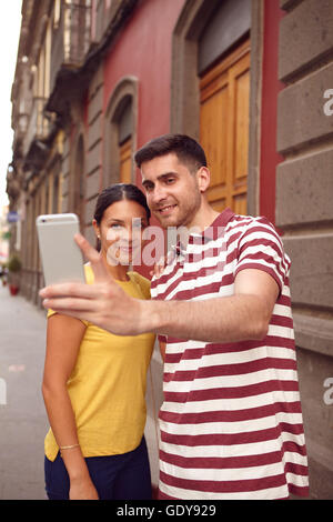 Süße junge Paar Blick auf Handy beim glücklich lächelnd, ein Selbstporträt zu nehmen lässig gekleidet in T-shirts mit alten Gebäuden Stockfoto