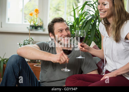 Paar trinken Rotwein im Wohnzimmer und lächelnd, München, Bayern, Deutschland Stockfoto