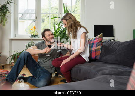Paar trinken Rotwein im Wohnzimmer und lächelnd, München, Bayern, Deutschland Stockfoto