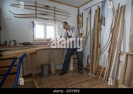 Männliche Bogenmacher rasieren Holz und gibt es eine Form des Bogens in Werkstatt, Bayern, Deutschland Stockfoto