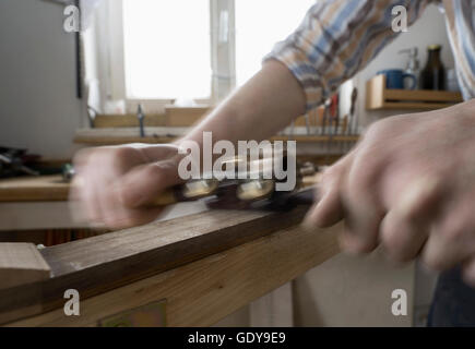 Männliche Bogenmacher rasieren Holz und gibt es eine Form des Bogens in Werkstatt, Bayern, Deutschland Stockfoto