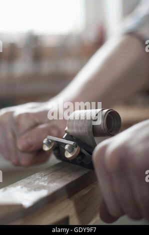 Männliche Bogenmacher rasieren Holz und gibt es eine Form des Bogens in Werkstatt, Bayern, Deutschland Stockfoto