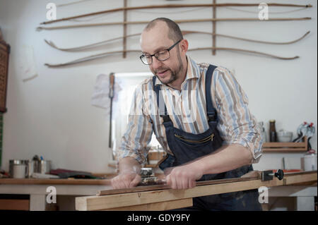 Männliche Bogenmacher rasieren Holz und gibt es eine Form des Bogens in Werkstatt, Bayern, Deutschland Stockfoto