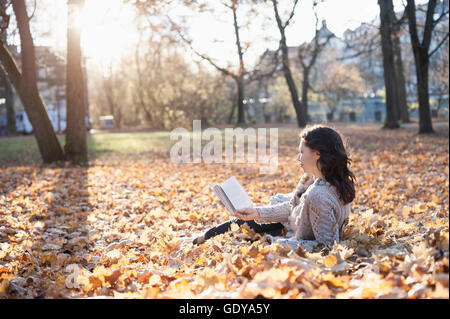 Reife Frau Buch liegend auf abgefallenen Blättern in den Park, Bayern, Deutschland Stockfoto