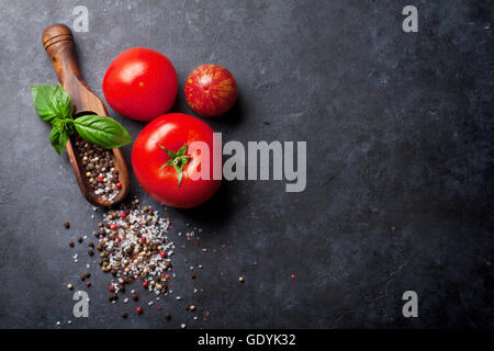 Pfeffer und Salz Gewürze, Kräuter Basilikum und Tomaten. Roten, weißen und schwarzen Pfeffer. Auf dunklen Steintisch. Draufsicht mit Textfreiraum Stockfoto