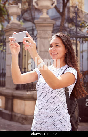 Niedliche junge Mädchen fotografieren mit ihrem Handy stehen im Vordergrund der alten Tore, tragen ihre Haare locker und eine gefleckte t Stockfoto