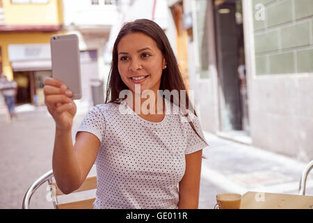Freudig lächelnd hübsches junges Mädchen in einem Straßencafé fotografieren beim tragen ihre Haare locker und legere Kleidung Stockfoto