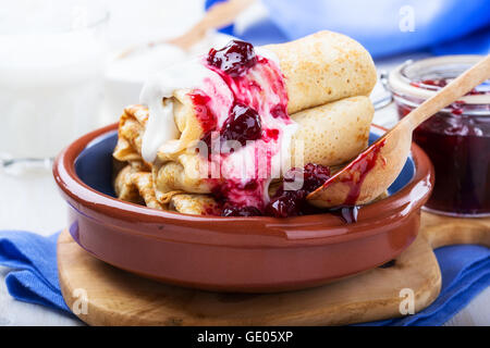 Hausgemachte Crepes-Rollen mit mit mit Quark Füllung serviert mit saurer Sahne und Beeren Marmelade Stockfoto