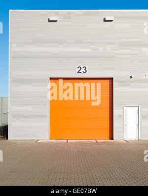 außen eine gewerbliche Lagerhalle mit einer orange Rolltor Stockfoto