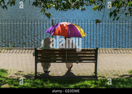 Zwei Frauen entspannen Sie im Schatten unter einem bunten Regenschirm bei hellem Sonnenschein. Stockfoto