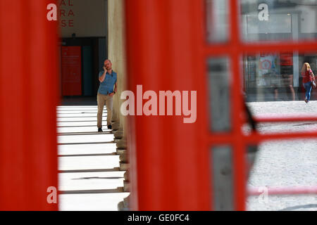 Ein Mann mit seinem Handy in Covent Garden, London, England. Betrachtet durch einen Spalt zwischen zwei roten Telefonzellen. Stockfoto