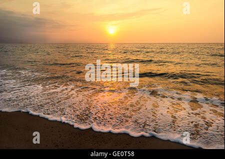 Meer Sonnenuntergang ist die untergehende Sonne wirft ein glänzenden goldenen Licht reflektiert das Wasser wie eine sanfte Welle ans Ufer Rollen. Stockfoto