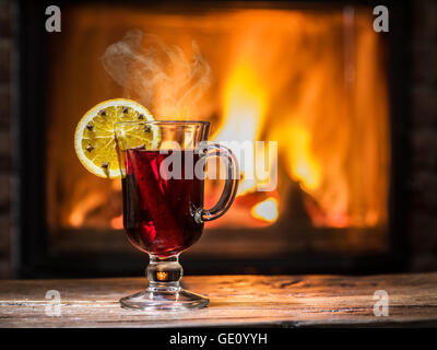 Glühwein mit Orangenscheibe, Nelken und Zimtstange. Kamin mit warmen Feuer im Hintergrund. Stockfoto