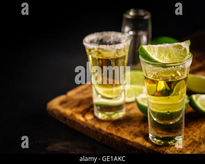 Zwei Gold Tequila Shots mit Kalk, Textfreiraum auf linken Seite. Gold mexikanische Tequila auf hölzernen Hintergrund. Alkohol trinken, selektive f Stockfoto