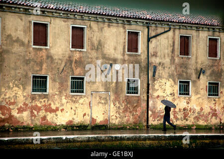 Ein Mann trägt und Regenschirm Spaziergänge entlang einer Terrakotta-Gebäude in Venedig, Italien Stockfoto