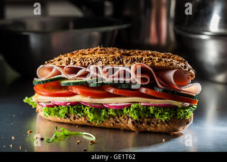 Sandwich mit Schinken, Käse, Tomaten, Gurken, Radieschen und Salat. Dunkel und launisch. Stockfoto