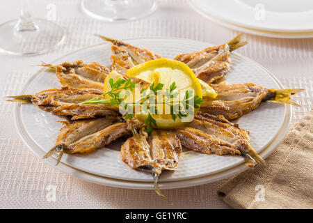 Gebratene Sardinenfilets serviert auf einem Teller mit Zitrone und Petersilie. Stockfoto