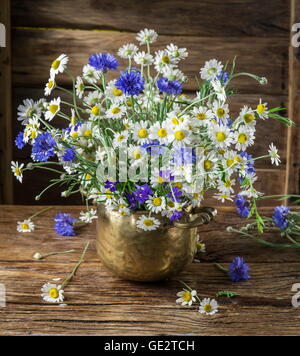 Bouquet von Kamillen und Kornblumen in der Vase auf dem Holztisch. Stockfoto