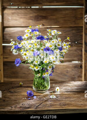 Bouquet von Kamillen und Kornblumen in der Vase auf dem Holztisch. Stockfoto