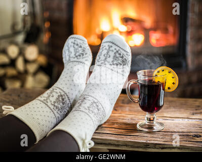 Wärmend und entspannend in der Nähe von Kamin. Frau Füße in der Nähe von der Tasse Glühwein am Kamin. Stockfoto