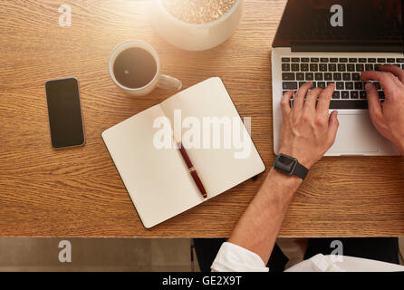 Draufsicht der Unternehmer arbeiten an seinem Schreibtisch. Moderner Arbeitsplatz mit Laptop, Smartphone, Tagebuch und Kaffee Tasse. Stockfoto