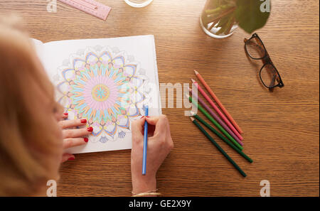 Nahaufnahme der weiblichen Zeichnung im Erwachsenen Malbuch mit Farbstiften auf Tisch zu Hause. Anti-Stress Erwachsene Malbuch. Stockfoto