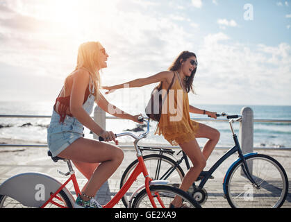 Aufnahme von zwei Freunden, für ein Fahrrad fahren auf einer Promenade. Junge Frauen auf Fahrrädern auf einer Küstenstraße an einem sonnigen Tag. Stockfoto