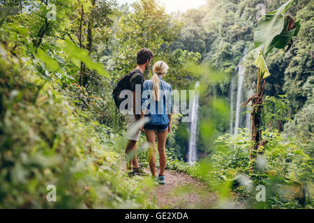 Rückansicht des junges Paar auf der Suche am Wasserfall. Zwei Wanderer im Wald stehen und Wasserfall anzeigen. Stockfoto