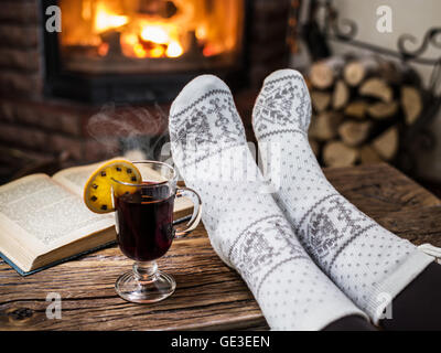 Wärmend und entspannend in der Nähe von Kamin. Frau Füße in der Nähe von der Tasse Glühwein am Kamin. Stockfoto