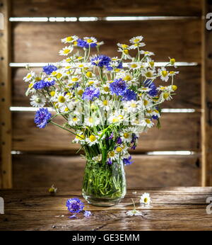 Bouquet von Kamillen und Kornblumen in der Vase auf dem Holztisch. Stockfoto