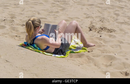 Eine junge Dame entspannt in der Sonne, lesen ein Buch am Strand von Bournemouth, UK Stockfoto