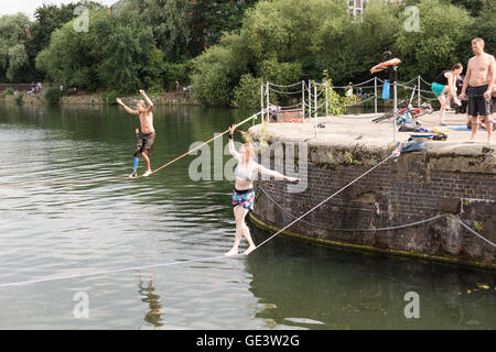 Shadwell, London. VEREINIGTES KÖNIGREICH. 23. Juli 2016. Menschen, die Slacklinen bei heißen, sonnigen Wetter in Shadwell Basin in Ost-London heute Nachmittag genießen. Slacklinen ist der Sport der balancieren auf einem Gurtband, das hoch über dem Boden befestigt, aber nicht zu straff gespannt. Menschen wurden gewarnt, nicht zum Schwimmen in Shadwell Basin, nachdem ein Mann ertrank und starb diese Woche. Bildnachweis: Vickie Flores/Alamy Live-Nachrichten Stockfoto