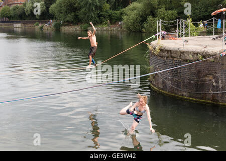 Shadwell, London. VEREINIGTES KÖNIGREICH. 23. Juli 2016. Menschen, die Slacklinen bei heißen, sonnigen Wetter in Shadwell Basin in Ost-London heute Nachmittag genießen. Slacklinen ist der Sport der balancieren auf einem Gurtband, das hoch über dem Boden befestigt, aber nicht zu straff gespannt. Menschen wurden gewarnt, nicht zum Schwimmen in Shadwell Basin, nachdem ein Mann ertrank und starb diese Woche. Bildnachweis: Vickie Flores/Alamy Live-Nachrichten Stockfoto