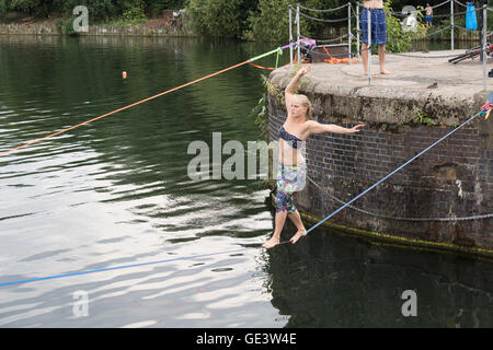 Shadwell, London. VEREINIGTES KÖNIGREICH. 23. Juli 2016. Menschen, die Slacklinen bei heißen, sonnigen Wetter in Shadwell Basin in Ost-London heute Nachmittag genießen. Slacklinen ist der Sport der balancieren auf einem Gurtband, das hoch über dem Boden befestigt, aber nicht zu straff gespannt. Menschen wurden gewarnt, nicht zum Schwimmen in Shadwell Basin, nachdem ein Mann ertrank und starb diese Woche. Bildnachweis: Vickie Flores/Alamy Live-Nachrichten Stockfoto