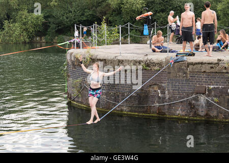 Shadwell, London. VEREINIGTES KÖNIGREICH. 23. Juli 2016. Menschen, die Slacklinen bei heißen, sonnigen Wetter in Shadwell Basin in Ost-London heute Nachmittag genießen. Slacklinen ist der Sport der balancieren auf einem Gurtband, das hoch über dem Boden befestigt, aber nicht zu straff gespannt. Menschen wurden gewarnt, nicht zum Schwimmen in Shadwell Basin, nachdem ein Mann ertrank und starb diese Woche. Bildnachweis: Vickie Flores/Alamy Live-Nachrichten Stockfoto