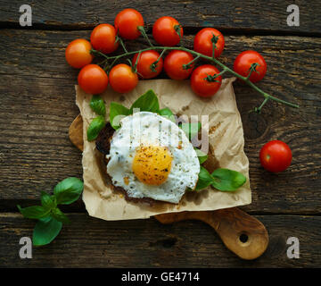 Rührei auf geröstetem Brot mit Basilikum, Gewürze und Cherry-Tomaten auf einem hölzernen Hintergrund Stockfoto