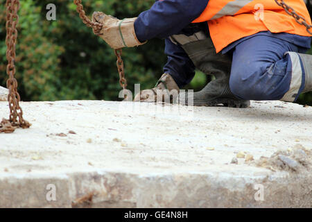 Arbeiter berührt die Kranhaken an den Schlaufen in der Betonplatte bei Reparaturarbeiten. Stockfoto