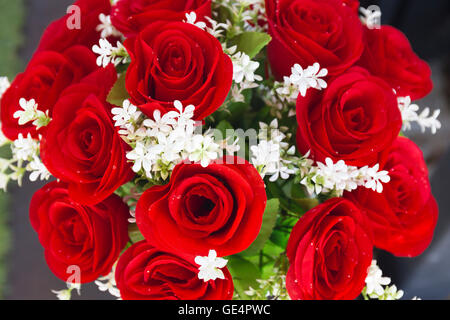 rote Rosen aus künstlichen Blumen und weiße Blumen in vase Stockfoto