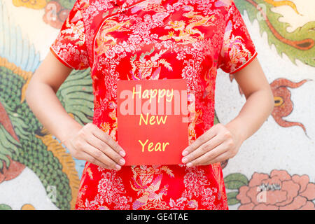 Frohes neues Jahr Asiatin mit roten Cheongsam hält ein rotes Paket wünschen Ihnen frohes neues Jahr auf chinesische Muster traditi Stockfoto