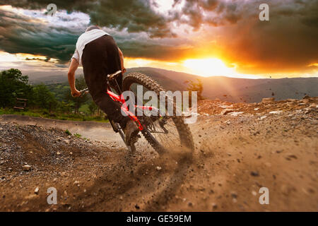 Mann auf Mountainbike fährt auf einen stürmischen Sonnenuntergang auf der Spur. Stockfoto